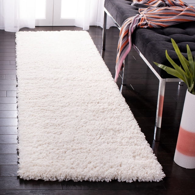 SAFAVIEH Fontana Jamie Tapis Shag Uni en Peluche Blanc avec pile Shag Synthétique en Peluche de 2 Pouces, Présenté comme un Coureur sur Plancher de Bois Franc Foncé à Côté d'Un Banc Noir avec un Jeté à Rayures et une Plante en Pot, Convient pour Ajouter Confort et style aux Couloirs Ou aux Entrées.