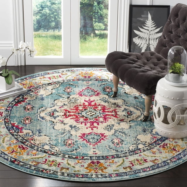 Safavieh Monaco Toria Tapis Traditionnel pour Aire, Rond avec un design Bohème-Chic Persan vibrant en Bleu, Rouge, Crème et Multicolore, Fabriqué en Polypropylène durable avec pile à Boucles Mixtes, Placé sur un Plancher de Bois Franc Foncé à Côté d'Une Chaise Capitonnée Brun Foncé et d'Une table d'Appoint en Céramique Blanche avec une cloche en Verre Plante, dans une Pièce Lumineuse avec de Grandes Portes en Verre Montrant un Décor Extérieur Vert. Il Convient Aussi pour Ajouter une Touche Colorée aux Coins Lecture Ou aux Aires de Détente.