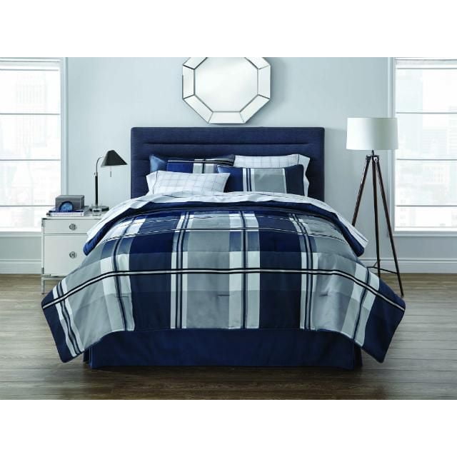 Springmaid Spencer Plaid Bed-in-a-Bag, 8 Piece in Queen and King, featuring a navy blue upholstered headboard and a plaid comforter in dark blue, grey, and white with corded piping. The set includes two shams, two pillowcases, fitted and flat sheets, and a bed skirt, ideal for a coordinated bedroom style.