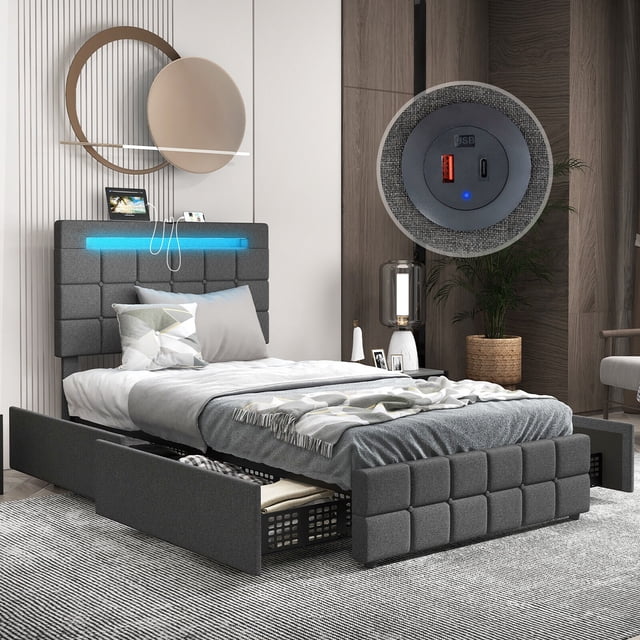 Gymax Twin Upholstered Platform Bed with LED Headboard Charging Station Storage Drawer in gray linen fabric. Features a tufted headboard with RGB LED lights offering 20 static colors and 22 dynamic modes, adjustable brightness, and flashing speeds controlled via remote. Includes a built-in charging station with two USB ports and an adjustable headboard height to fit 8-12 inch mattresses. The bed frame has four large storage drawers on casters for easy access and is supported by solid wooden slats and metal legs for durability, with a weight capacity of 880 lbs. Shown in a modern bedroom setting with a neatly made bed and partially open storage drawer.