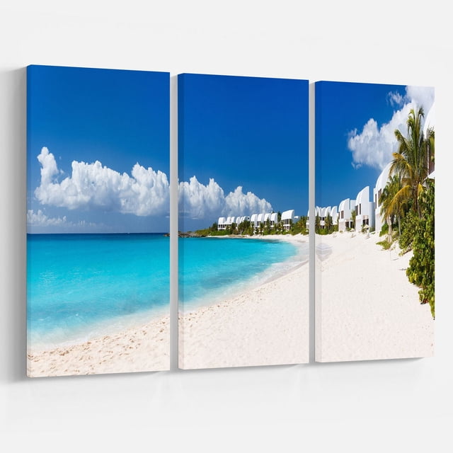 Design Art Caribbean Beach Panorama Canvas Print featuring a three-panel gallery wrapped cotton canvas with a panoramic view of a white sandy beach, turquoise ocean, and modern white beachfront buildings under a bright blue sky with clouds, ready to hang wall art suitable for home décor and office spaces.