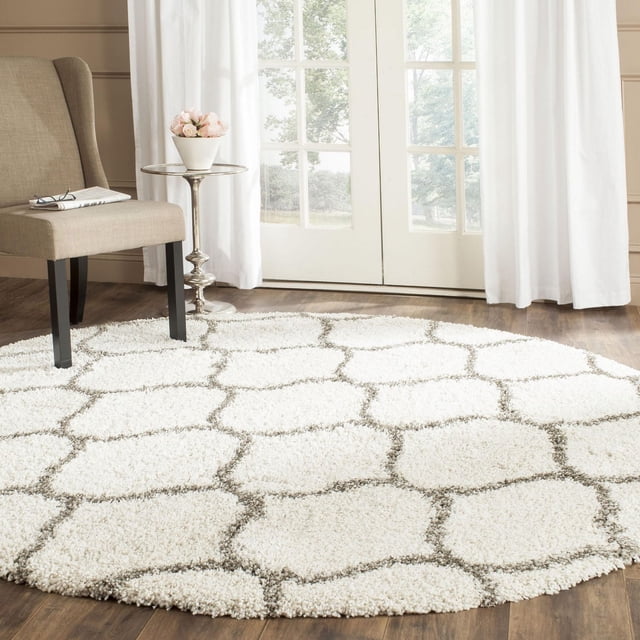 Safavieh Hudson Tapis Shag Géométrique Arline, Rond avec une Épaisse pile Shag Ivoire et un Motif de Carreaux Gris Pâle en Forme d'Oignon, Posé sur un Plancher de Bois Près d'Une Chaise beige et d'Une table d'Appoint Argentée avec des Fleurs Roses, Convient pour Ajouter de la texture aux Salons Modernes.