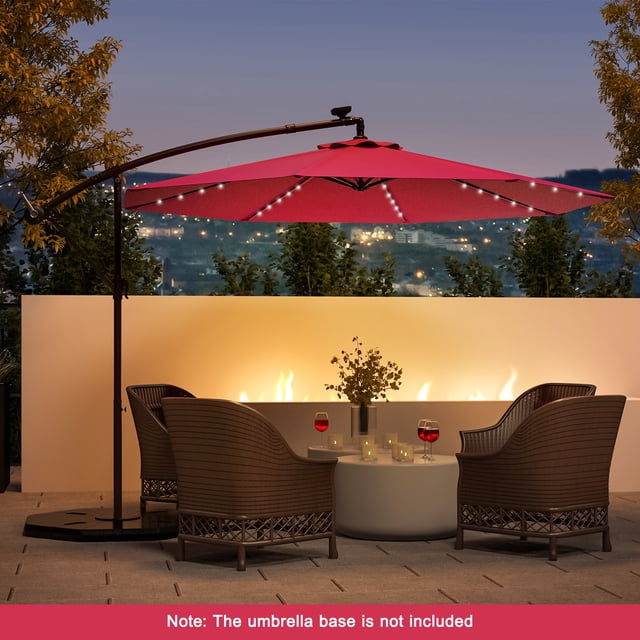 Costway 10 Ft Patio Solar LED Offset Umbrella in wine color with 40 LED lights, featuring a wide 10-foot polyester canopy supported by a sturdy steel frame and cross base. The umbrella is shown in an outdoor evening setting, illuminating a patio area with wicker chairs and a round table. Note: The umbrella base is not included.