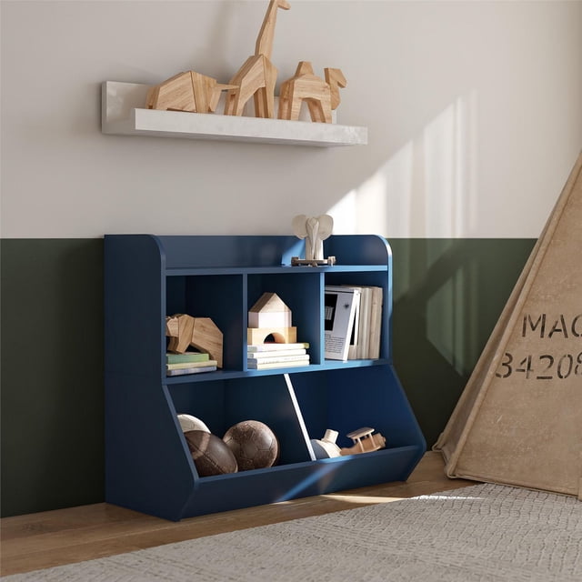 DOREL KIDS STORAGE navy blue toy storage unit with five open compartments holding children's books, wooden toys, and balls, placed against a two-tone green and beige wall in a child's room with a beige play tent and wooden animal figurines on a white floating shelf above.