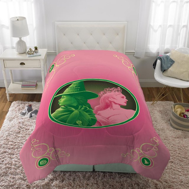 Wicked « We Are Unlimited » Couette Format Simple/double en Rose Microfibre 100 % polyester avec un design Ovale central Montrant des Profils Verts et Roses de Deux Femmes, l'Une Portant un Chapeau de Sorcière et l'Autre un Diadème, Accentuée de Tourbillons Dorés. Lavable à la Machine et Résistante aux Plis, Exposée sur une Tête de Lit Capitonnée Blanche dans une Chambre Éclatante avec une Table de Nuit et une Chaise Blanches.