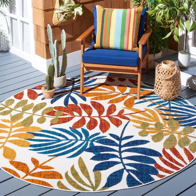 SAFAVIEH Cabana Elouise Floral Indoor/Outdoor Area Rug, round with multicolored leaf patterns in blue, orange, red, and green on white, placed on a gray deck floor with a wooden armchair with blue cushions and a striped pillow, surrounded by potted cacti, leafy plants, and a woven lantern, ideal for patios or sunrooms.