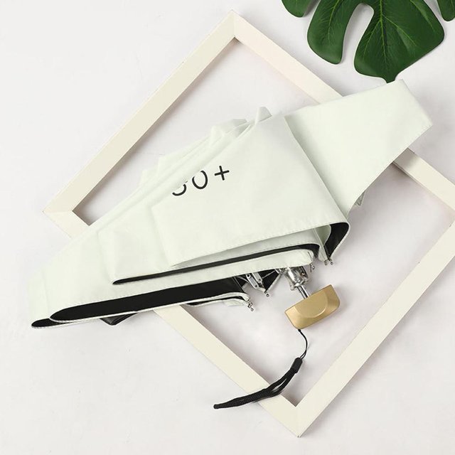 Mini Pocket Umbrella Ultralight 5-Fold Portable Folding UV Protection Small, designed as a compact travel accessory. The umbrella is shown folded with a light-colored impact cloth canopy marked '50+' for UV protection. It features a durable PP handle with a wrist strap, ideal for both sunny and rainy days.