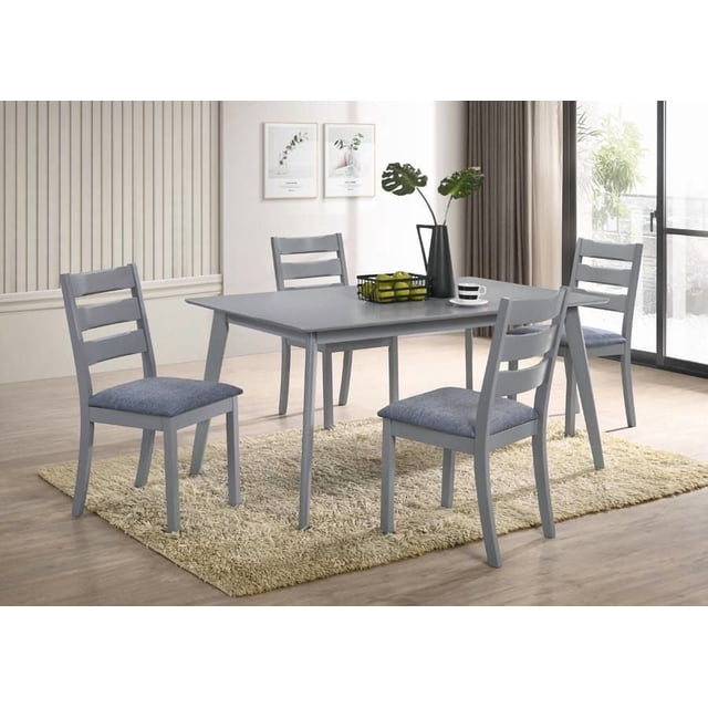 Aerys Tommy Solid wood Dining Table Set with 4 Dining Chairs in Grey featuring a rectangular solid wood table and four ladderback chairs with grey upholstered fabric seats, placed on a beige shag rug in a bright dining room with light wood flooring, neutral walls with botanical prints, and a large window with curtains. This compact set is ideal for apartments and kitchen spaces.