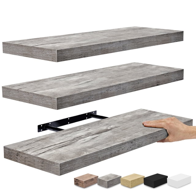 Sorbus Wall Mounted Floating Shelves for Wall Décor, a set of three large 24-inch gray shelves with a faux wood matte finish. The image shows the rectangular shelves in a staggered arrangement, highlighting their smooth texture and sturdy design. One shelf is being installed with a visible mounting bracket. Ideal for displaying decorative items, photo frames, or plants, these shelves complement modern, farmhouse, or boho interiors. Dimensions are approximately 23.75 inches long by 9.25 inches wide.