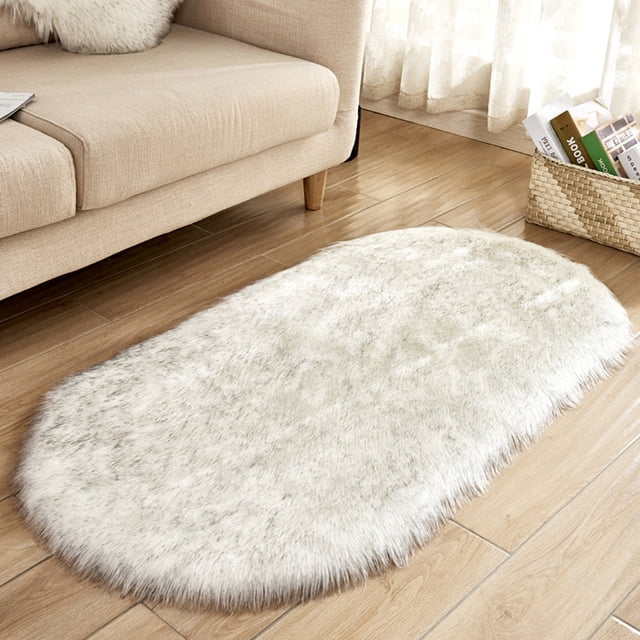Agiferg Super Soft Faux Sheepskin Area Rug, 40x60 cm, ideal for bedroom or living room decor. The oval-shaped shaggy plush carpet features a light neutral faux sheepskin texture, placed on a wooden floor near a beige sofa and a woven basket, suitable as an accent rug or bedside rug.