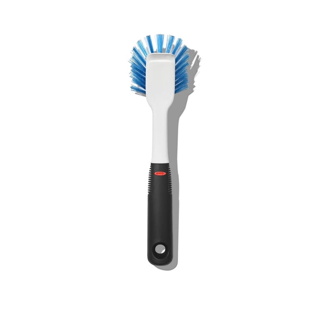 OXO Softworks dish brush with a white neck and black non-slip handle featuring a red OXO logo, blue stiff nylon bristles in a flared shape, and a built-in scraper for removing baked-on food, ideal for cleaning cookware and bakeware.