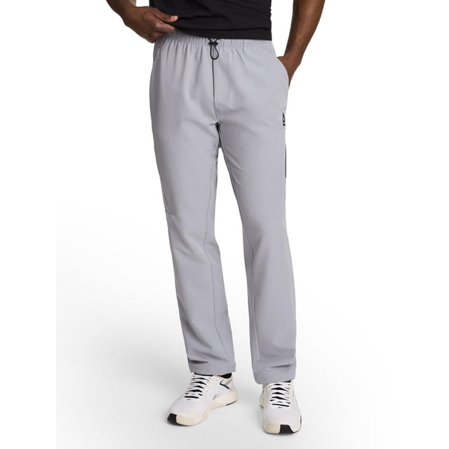 Reebok Men’s Swiftmotion Woven Jogger in light grey with a slim fit and 31-inch inseam, crafted from stretch performance woven fabric with moisture-wicking and breathable mesh details, featuring an elastic bungee cord waistband, side seam pockets, and a zippered pocket on the left leg, shown worn with white athletic shoes, suitable for gym workouts and casual wear.