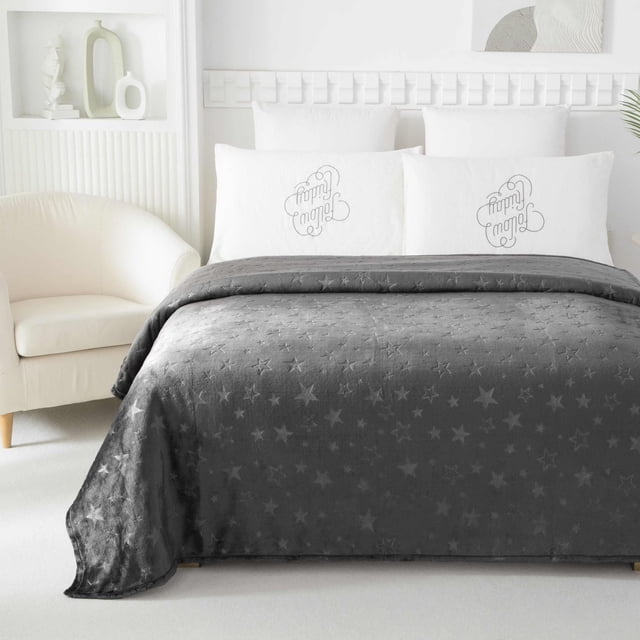 Mainstays Kids Embossed Blanket Stars in grey with embossed star patterns, spread over a bed with white pillows embroidered with 'Love Family' text, featuring a soft plush polyester blend texture in a bright, minimalist bedroom with a cream armchair and white decorative shelf.