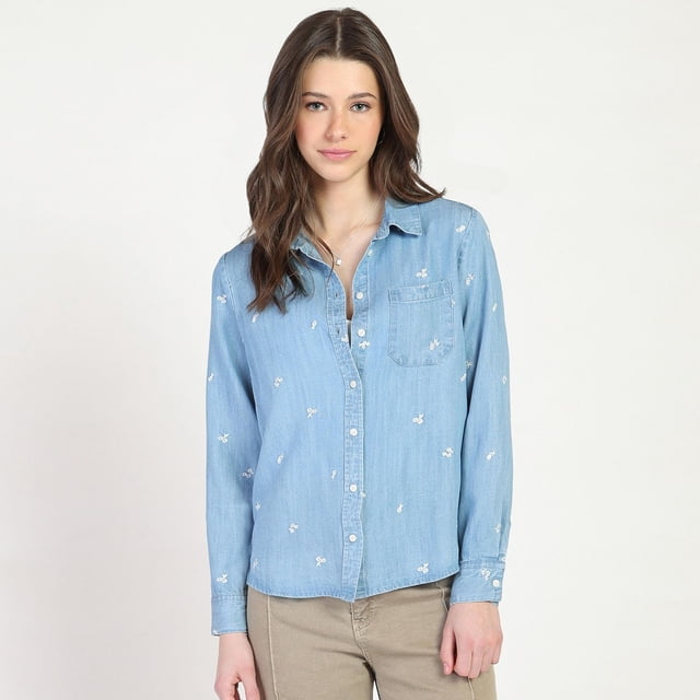 Bloom Girl Embroidered Button Front Shirt in light blue denim with small white embroidered flowers, featuring a classic collar, button-front closure, long sleeves with button cuffs, and a chest pocket, worn with beige trousers. Made of 100% TENCEL with a relaxed fit, suitable for layering over casual tops.