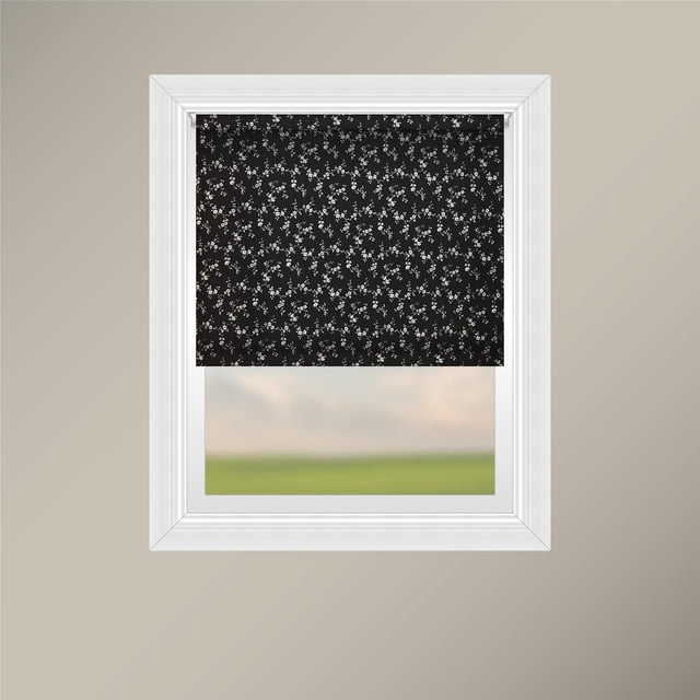 Off Cut Shades Chainless Sheer Roller Shade with black polyester fabric featuring a white floral pattern, displayed in a centered front view inside a white window frame on a beige wall. This roller blind provides light filtering and privacy, ideal for home window coverings with easy chainless operation for child and pet safety.