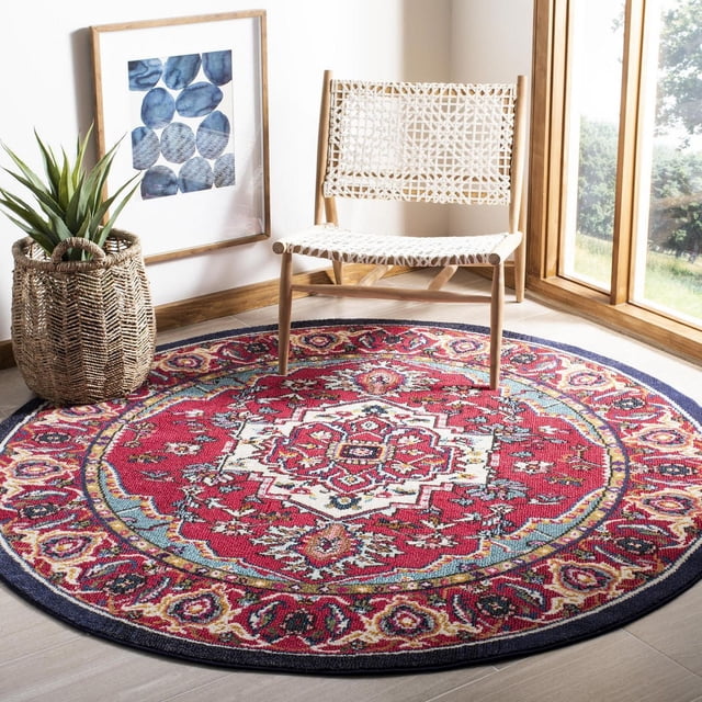 Safavieh Monaco Vivyan Traditional Area Rug, round with vibrant red and blue Persian-inspired patterns, made of durable polypropylene with mixed loop pile, placed on light wood flooring near a woven white chair, framed blue leaf artwork, and woven basket planter with green plant by a window. Often used to add Bohemian-chic style to home interiors.