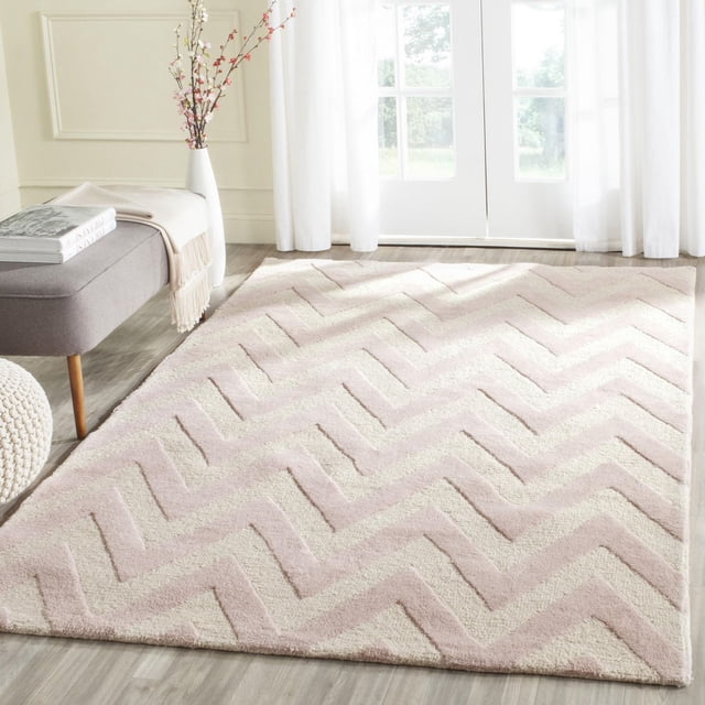 Safavieh Cambridge Kaitlyn Zig Zag Stripes Area Rug featuring hand-tufted wool with plush cut and high/low loop piles in a beige and cream zig zag pattern, placed on light wood flooring in a bright room with a gray bench, white vase with branches, and sheer white curtains, ideal for adding texture and warmth to home or office spaces.