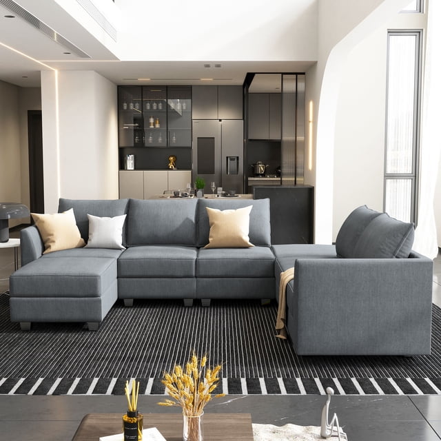 HONBAY Modular Sectional Sofa avec Chaises et Ottomans Réversibles en Forme de U, Illustrés en Tissu Gris Bleuâtre. le Sofa Présente un Cadre en Bois Massif, un Rembourrage en Éponge Haute Densité et un Rembourrage 100 % polyester. Il Comprend un Rangement Caché sous Chaque Siège et des sections Modulaires Pouvant Être Réorganisées pour s'Adapter à Diverses Aménagements. Exposé dans un Salon Moderne avec un Tapis Rayé Noir et Blanc et une Cuisine Contemporaine en Arrière-Plan.