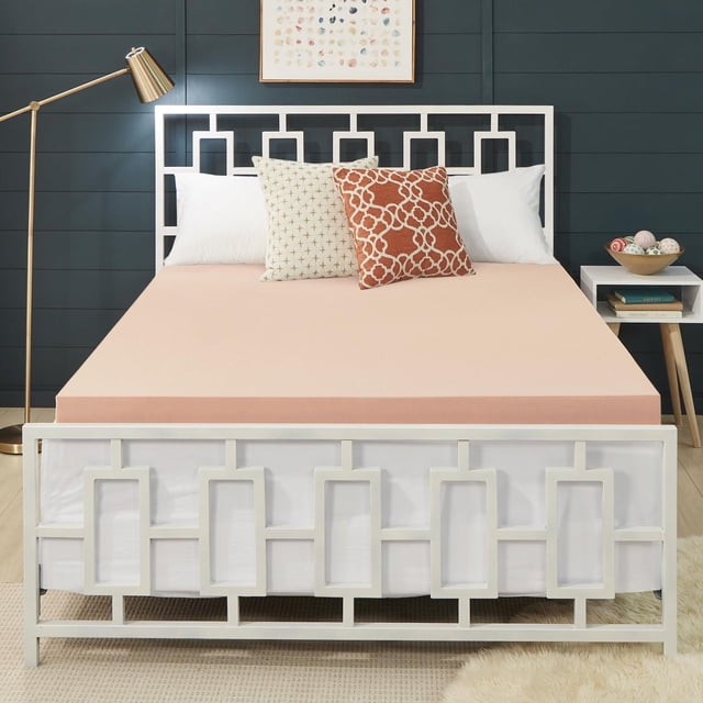 Dream Serenity 3" COPPER RX Memory Foam Mattress Topper, Double, on a white metal bed frame with geometric rectangular patterns, topped with white and decorative beige and rust pillows, set against a dark blue paneled wall with framed abstract art, beside a gold floor lamp and white nightstand with books and decorative balls, featuring breathable, pressure-relieving comfort and antimicrobial copper infusion.