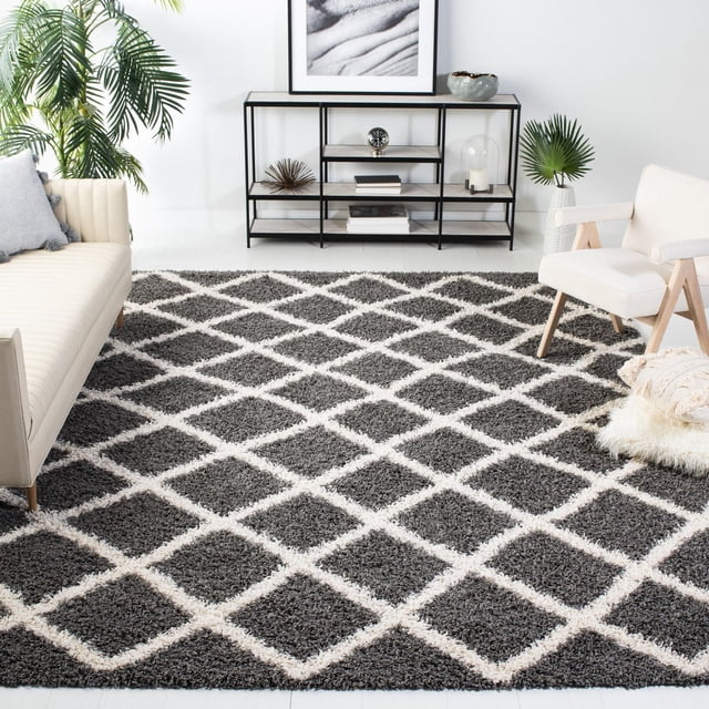 Safavieh Dallas Jerrie Geometric Shag Area Rug featuring a plush diamond pattern in dark gray and white, placed in a contemporary living room with a cream sofa, white armchair, black metal and wood shelving, and green plants, ideal as an accent rug for high-traffic areas.