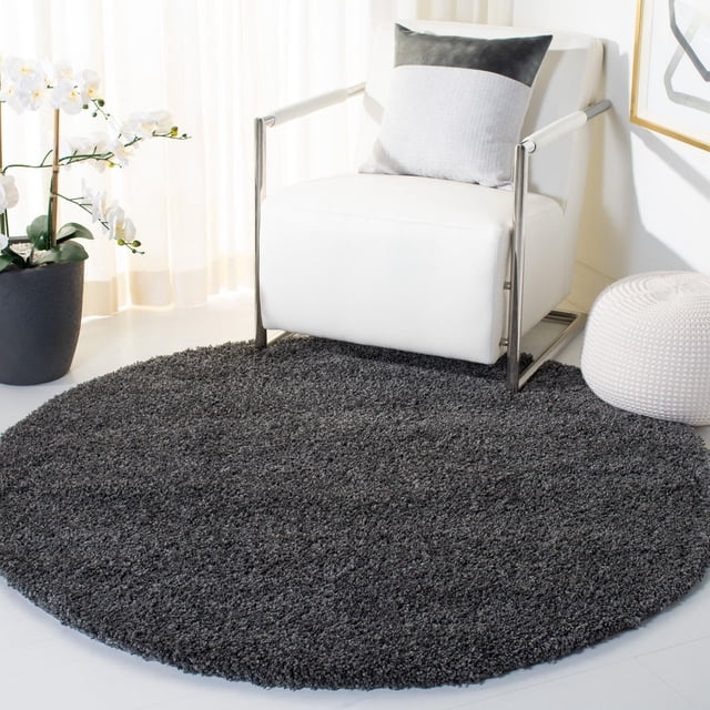 Safavieh California Solid Plush Shag Area Rug, round with a dense 4.5kg/m² polypropylene pile in dark grey, placed in a bright room under a white leather armchair with chrome arms, beside a white knitted pouf and a black pot with white orchids, suitable for adding plush texture to modern home interiors.