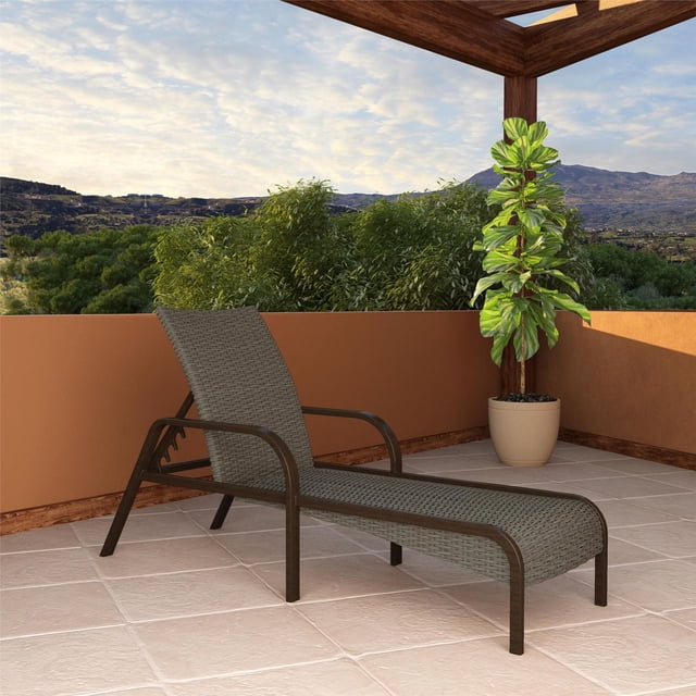COSCO Outdoor Living SmartWick patio chaise lounge in dark brown resin wicker with weather-resistant steel frame and faux wood finish, set on a tiled outdoor patio under a wooden pergola next to a potted green plant, with mountain views in the background.