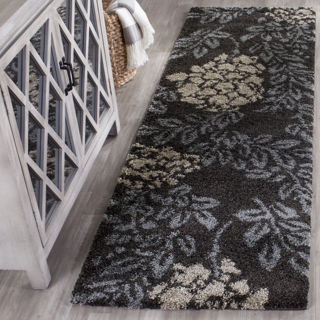 Safavieh Florida Benton Floral Shag Area Rug runner with a dark charcoal background and beige and gray floral vine patterns in a plush high-low pile, placed on a light wood floor beside a gray cabinet and woven basket, ideal for adding texture and warmth to narrow hallways or entryways.