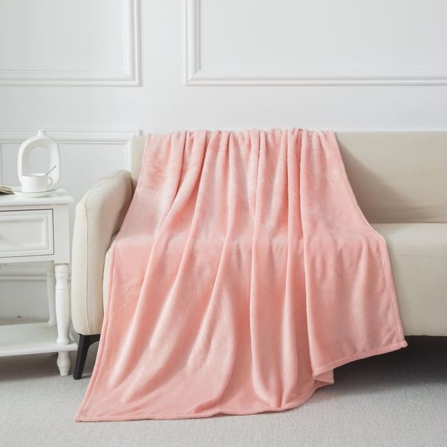Mainstays Plush Throw Pink draped over a beige sofa, showing its soft, plush polyester fabric and solid pink colour, measuring 50 in. by 60 in., suitable as a cozy throw blanket for home bedding and living areas.