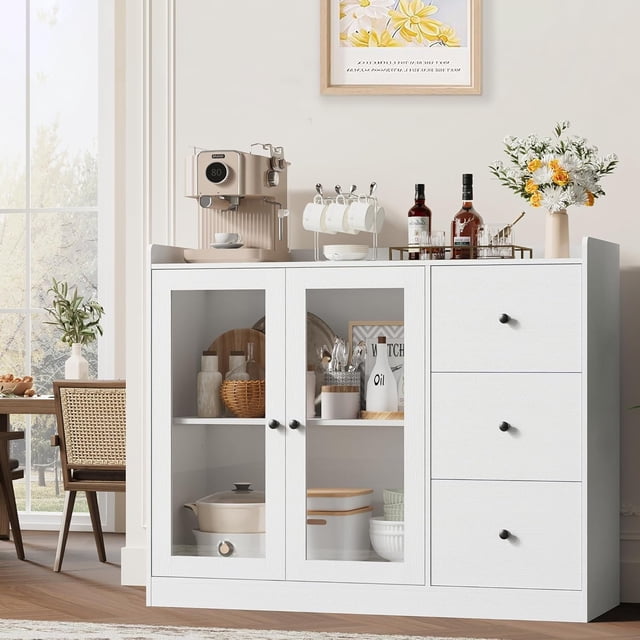 Garvee Sideboard Buffet Cabinet with Storage, 43-inch coffee bar cabinet in white featuring three drawers, two glass doors with adjustable shelves, and a spacious tabletop. The cabinet is styled in a bright dining room setting with decor items, a coffee machine, and bottles on top. Transparent glass doors reveal neatly organized kitchenware inside.