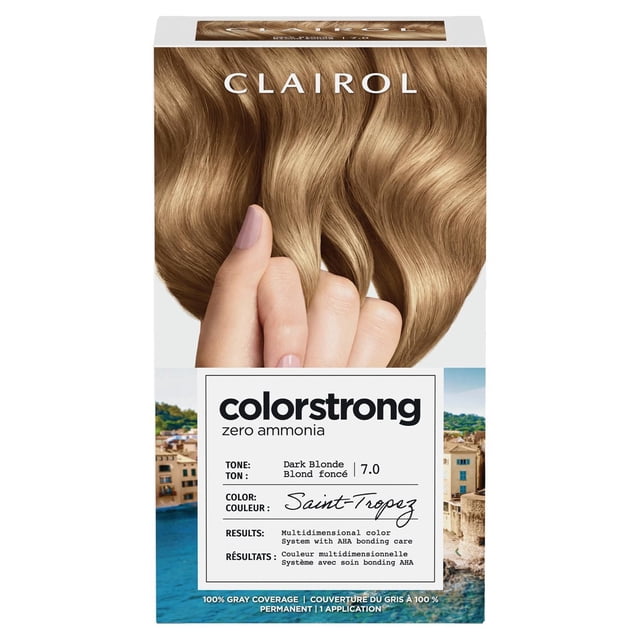 ColorStrong Permanent Hair Dye by Clairol in Dark Blonde 7.0 Saint-Tropez shade with zero ammonia and AHA bonding system for multidimensional color and 100% gray coverage, packaging features hand holding smooth, wavy dark blonde hair strands over a coastal town background.