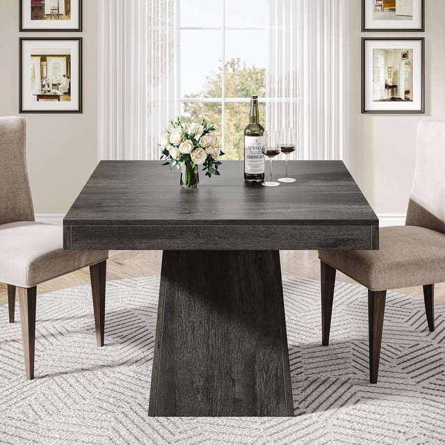 Tribesigns Square Dining Table for 4, 31.5-inch kitchen table with a sturdy pedestal base, shown in a rustic farmhouse design with a gray wood grain finish. The table is set in a bright dining room with two beige upholstered chairs, a vase of white flowers, and wine glasses on the tabletop. Ideal for small spaces, it accommodates up to four people and offers versatile use as a dining, coffee, or game table.