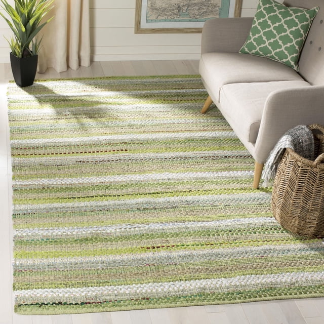 Safavieh Montauk Darion Striped Area Rug on light hardwood floor, featuring flat-weave cotton with horizontal green, beige, and white stripes. Placed next to a beige sofa with a green patterned pillow and woven basket, ideal for coastal and contemporary runner rug décor.