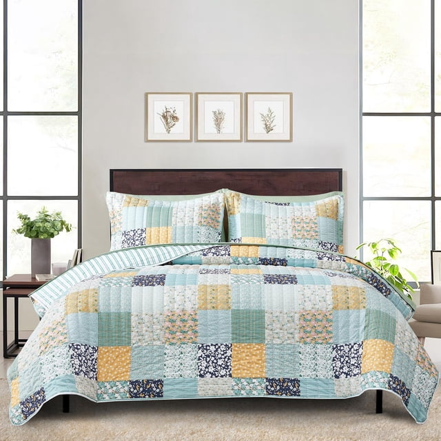 Mainstays Quilt-in-a-Bag Bedding Set on a bed with a dark wood headboard in a bright bedroom. The lightweight quilt and matching pillow shams feature a patchwork pattern in pastel blue, yellow, green, and navy with floral and geometric prints. Made from 55% recycled polyester, the set includes a quilt, sheets, pillowcases, and a storage bag. The room has large windows, a beige carpet, a side table with a plant, and three framed botanical prints above the bed. This bedding set is suitable for year-round comfort and easy machine washing.