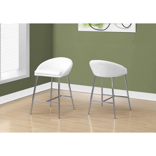 Monarch Specialties bar stool set of 2, counter height kitchen seating with white PU leather-look cushioned seats and low curved backs, supported by chrome metal legs with footrests, placed on light wood flooring against olive green walls. Suitable for small eat-in spaces or lofts.