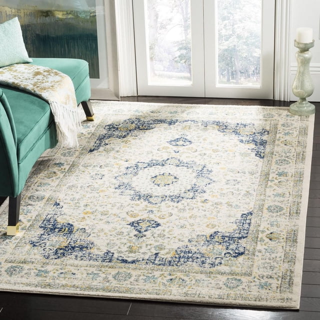 SAFAVIEH Evoke Teale Traditional Area Rug featuring a soft frieze texture and a traditional pattern in muted blue, cream, and gold tones, laid on dark hardwood flooring in a bright room with glass doors, partially under a teal sofa with gold-accented legs and a light throw, ideal for durable and stylish living room decor.
