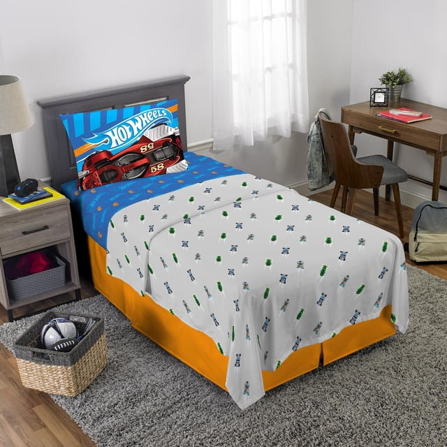 Hot Wheels "Fast Pace" twin sheet set on a twin bed with a blue fitted sheet featuring the Hot Wheels logo, a grey flat sheet with race car patterns, and a reversible pillowcase showing vibrant race car designs, made of 100% polyester microfiber and machine washable, suitable for kids' bedding.