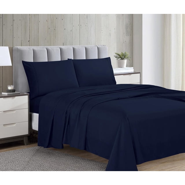 Ensemble de Draps en Microfibre Série 1800 Bleu Marine sur un Lit avec une Tête de Lit Rembourrée Gris Pâle, Incluant un Drap Plat, un Drap-Housse à Bords Élastiques et Deux Taies d'Oreiller en Tissu Microfibre Doublement Brossé, Doux et Résistant aux Plis. la Chambre Présente des Parois en Panneau de Bois Clair, un Tapis Gris, des Tables de Nuit Blanches avec Tiroirs, une Lampe Blanche et une Petite Plante en Pot.