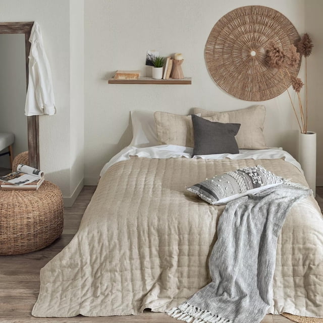 Bouclair Beige Quin Collection - Ensemble Couvre-Lit 3 Pcs Très Grand Présenté dans une Chambre Sereine. l'Ensemble Comprend une Courtepointe Beige Texturée et Deux Taies d'Oreiller Assorties Faites de 80 % polyester et 20 % Lin. les Dimensions Sont 92 Pouces de Large par 108 Pouces de Haut. Stylé avec des Tons Neutres, une Déco Murale Tissée et un ottoman en Rotin, Cet Ensemble de Literie Très Grand Favorise la Détente.
