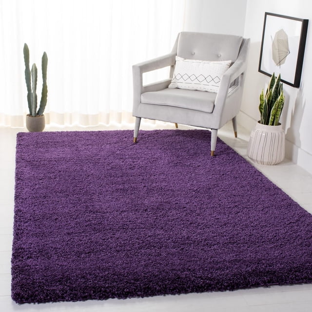 Safavieh Milan Harlow Tapis Shag Uni en texture Peluche Riche Violet sur Plancher de Bois Franc Clair, Assorti à un Fauteuil Moderne Gris Pâle avec un Coussin Lombaire Géométrique Blanc, Près d'Un Grand cactus dans un pot beige par des Rideaux Blancs Transparents, et une Plante Serpent dans un pot en Céramique à Rayures Blanches sous Cadre art Mural Géométrique, Idéal comme Tapis d'Accent pour la Déco Contemporaine de la Maison.