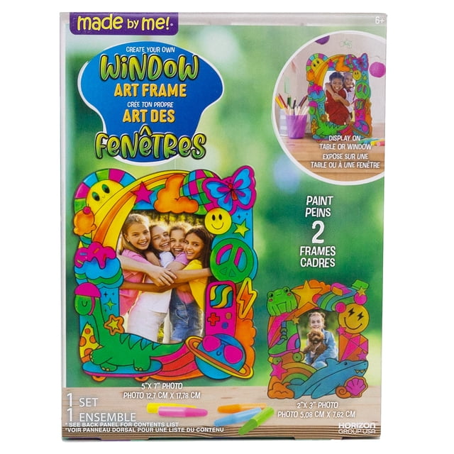 Made By Me Create Your Own Window Art Frame kit featuring two colorful, playful photo frames with designs including stars, smiley faces, peace signs, and animals, sized for 5x7 and 2x3 inch photos, ideal for kids craft kits and window paint activities, shown with paint tubes on a green background.