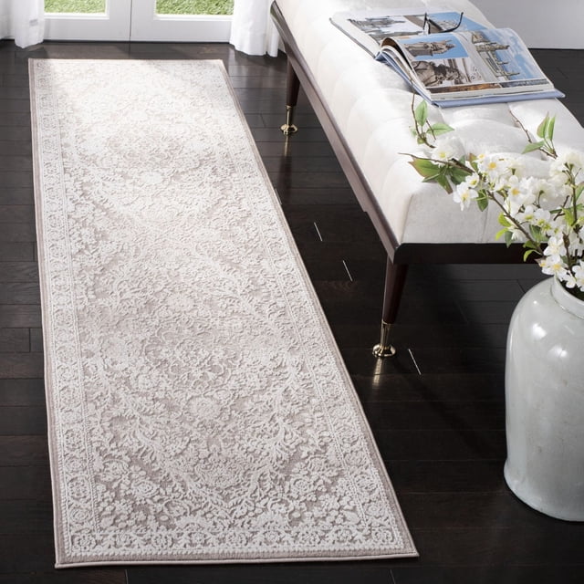 SAFAVIEH Reflection Alayna Traditional Area Rug in beige with intricate floral motifs and raised cut pile texture, placed on dark hardwood flooring beside a cream upholstered bench with brass-capped legs and a vase of white flowers, suitable for adding warmth and elegance to runner rug spaces.