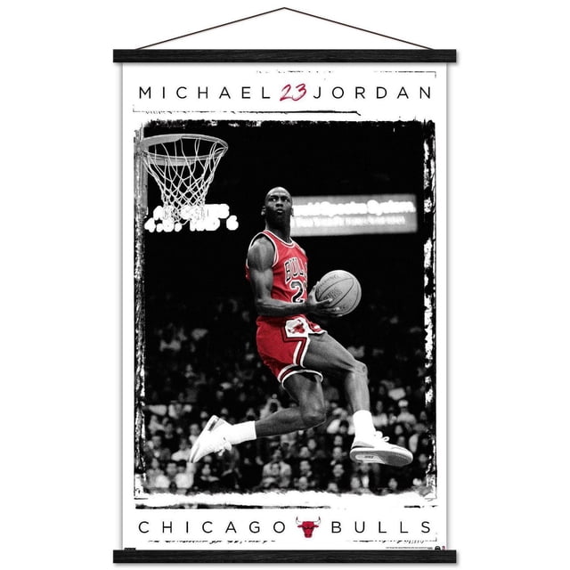 Michael Jordan - Dunk Wall Poster, 14.725" x 22.375" framed showing Michael Jordan in a red Chicago Bulls jersey number 23 performing a basketball dunk mid-air near the hoop, wearing white Nike shoes, with a black and white crowd background and bold text 'MICHAEL 23 JORDAN' above and 'CHICAGO BULLS' with the team logo below, suitable for sports room or office wall decor.