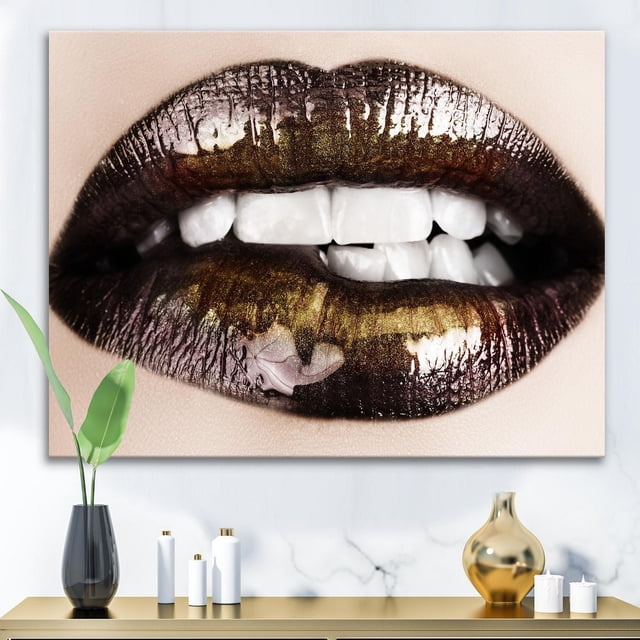 Designart Black Gold Lips Biting Canvas Wall Art depicting a close-up of lips with black and gold metallic lipstick biting the lower lip, printed on premium cotton canvas with gallery-wrapped edges, ready to hang above a modern console table with decorative vases and candles, suitable for contemporary home décor.