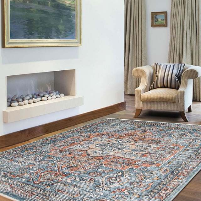 ECARPET Traditional Distressed Ultra Soft Area Rug Bahama Heriz Collection on hardwood flooring, featuring a rectangular rug with a vintage Heriz pattern in distressed blue, orange, and beige tones. The rug is placed near a beige upholstered armchair with a striped cushion, a modern built-in fireplace with decorative stones, and neutral curtains, suitable for enhancing indoor living spaces with durable, classic style.