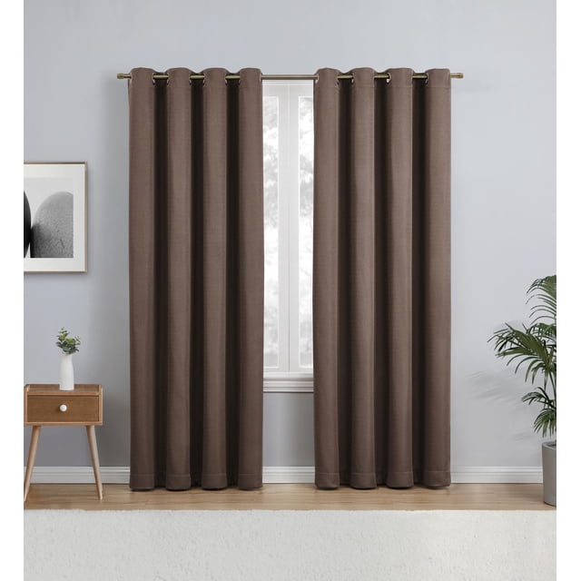 Eclipse Heath 63" Grommet Blackout Window Curtains Panel in mushroom color hanging on a metal rod in a modern room with light grey walls, wooden floor, a small wooden side table with a white vase and plant, and a potted palm plant, designed to reduce light, noise, and help with energy savings while providing privacy.