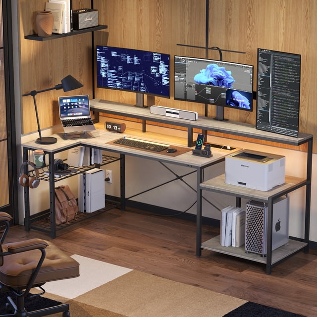 Bestier 71 inch L-Shaped Gaming Desk in grey with a spacious corner design, ergonomic monitor stand, adjustable storage shelves, and built-in power outlets. Features RGB LED lights, a cup holder, and a headphone hook, suitable for gaming or office setups. Displayed in a modern workspace with multiple monitors, a laptop, and organized accessories, emphasizing its functionality as a computer desk and office furniture.