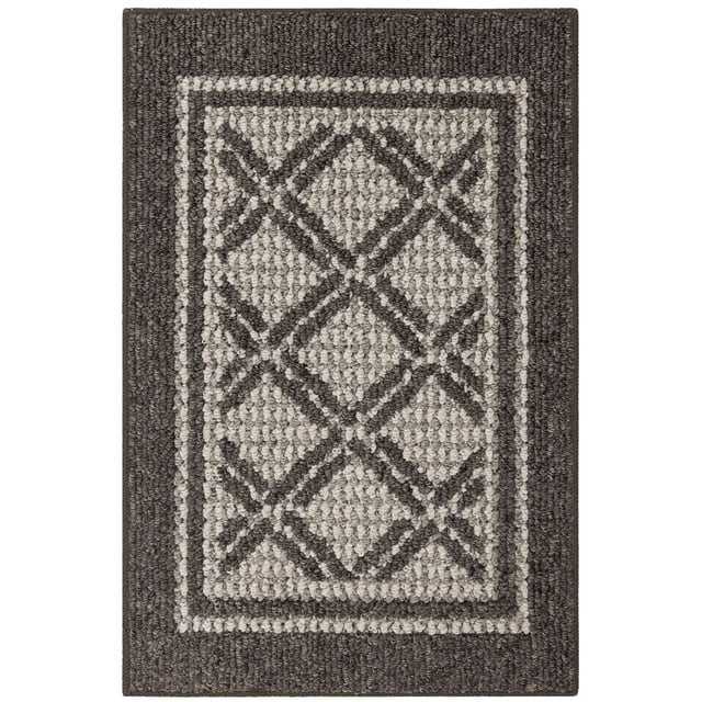 Hometrends Shefield Polyester Accent Rug with a geometric diamond lattice pattern in grey tones and black borders, tufted with moisture, stain, and fade-resistant olefin yarn, designed for high-traffic indoor spaces like kitchens, entryways, and laundry rooms, featuring a low-profile pile to prevent door obstruction.