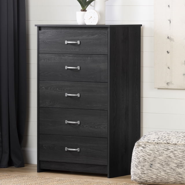 South Shore Tassio 5-Drawer Chest for Adult in gray oak finish with five drawers featuring metal handles and rigid metal slides for durable storage, placed in a bedroom with light wood floor, white shiplap wall, black curtain, and decorative items on top; suitable for organizing clothes and accessories.