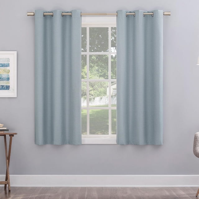 Mainstays Cooper Blackout Window Curtains Panel in light blue with classic woven texture and blackout technology, featuring metal grommets for curtain rods up to 1.5 inches diameter, hanging in a room with light grey walls and wooden floor, framing a window with a green outdoor view, ideal for privacy and thermal insulation.