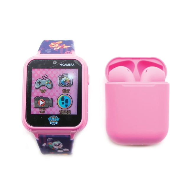 Paw Patrol Touch Screen Interactive Watch with Bonus Earbuds showing a pink digital watch with touch screen icons for games, camera, video, and pedometer, paired with a pink charging case holding matching earbuds and a purple strap decorated with Paw Patrol characters, suitable for children aged 6 and up.